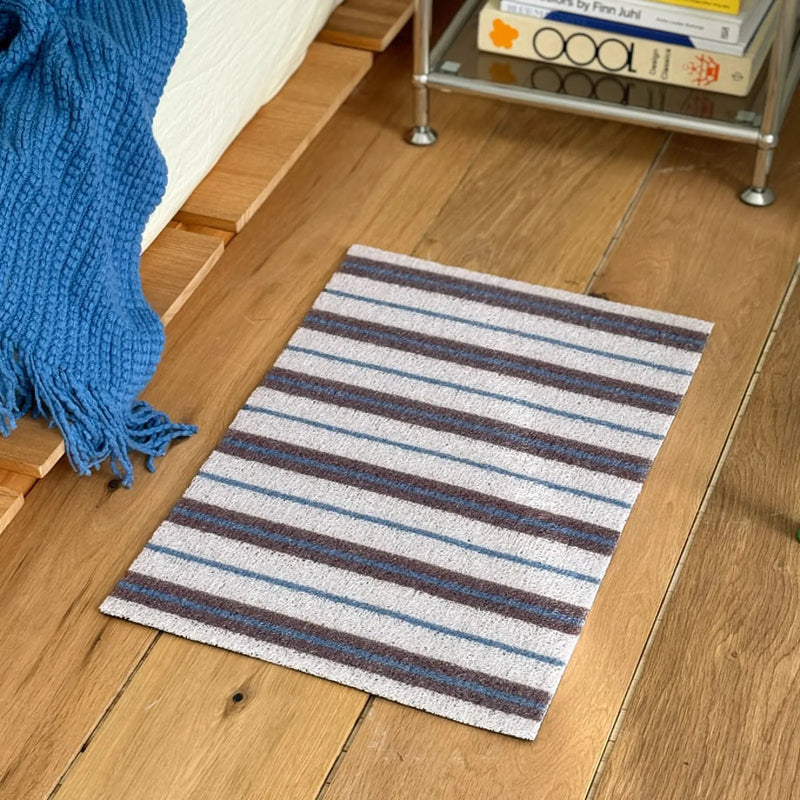 Mist white PVC coil rug with blue and purple pinstripes on a wooden floor - RoomDen