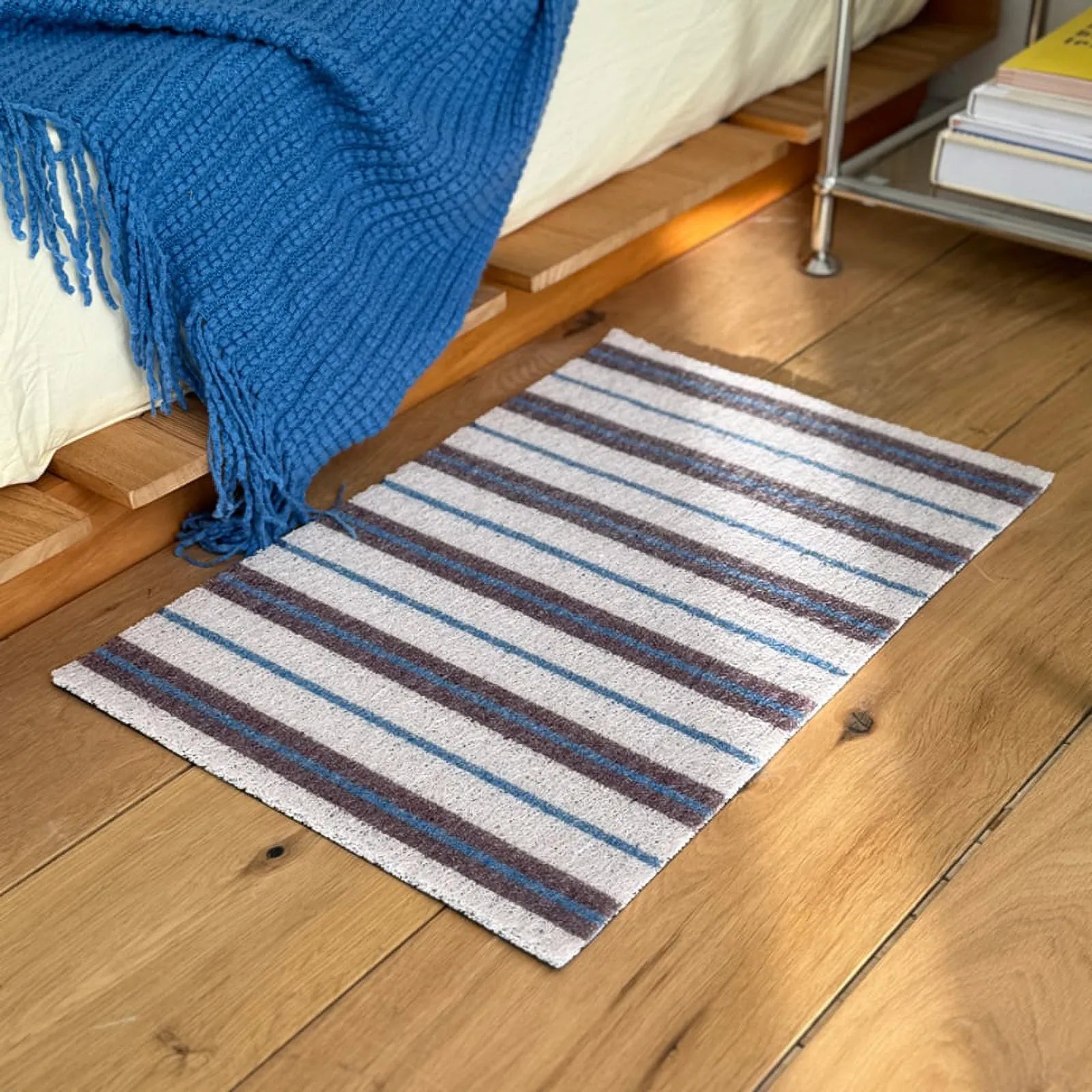 Angled view of the white minimalist striped entrance mat next to a blue blanket.