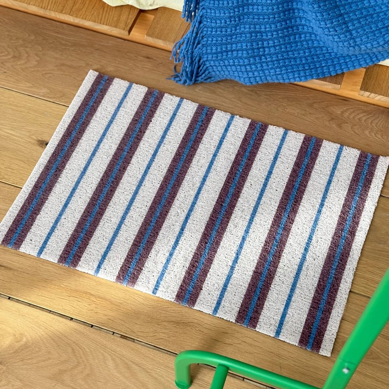 RoomDen white striped PVC mat styling shot with blue textile and green furniture leg.