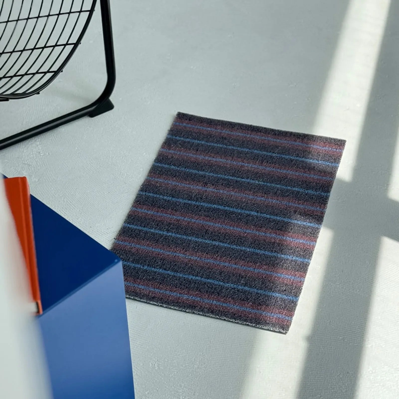 Perspective view of the dark grey modern striped entrance rug next to blue furniture.