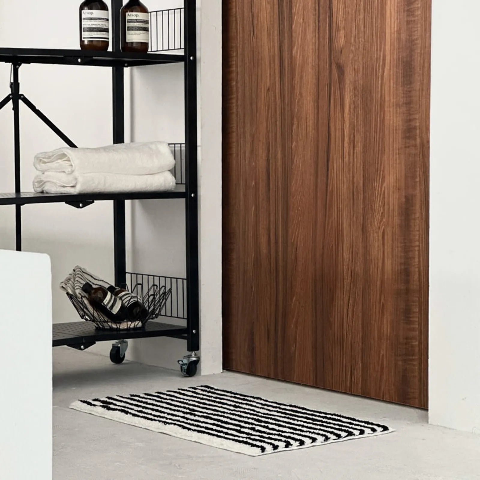 Black and white wavy striped rug placed near a walnut door and shelf - RoomDen
