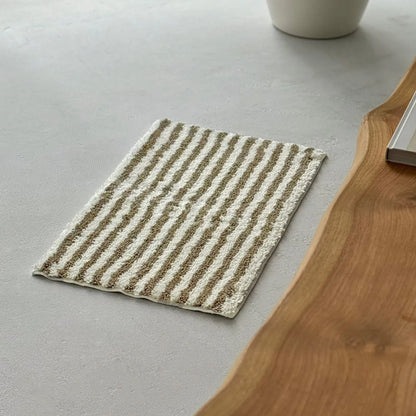 Olive wavy rug styled on floor next to a wooden bench and plant - RoomDen