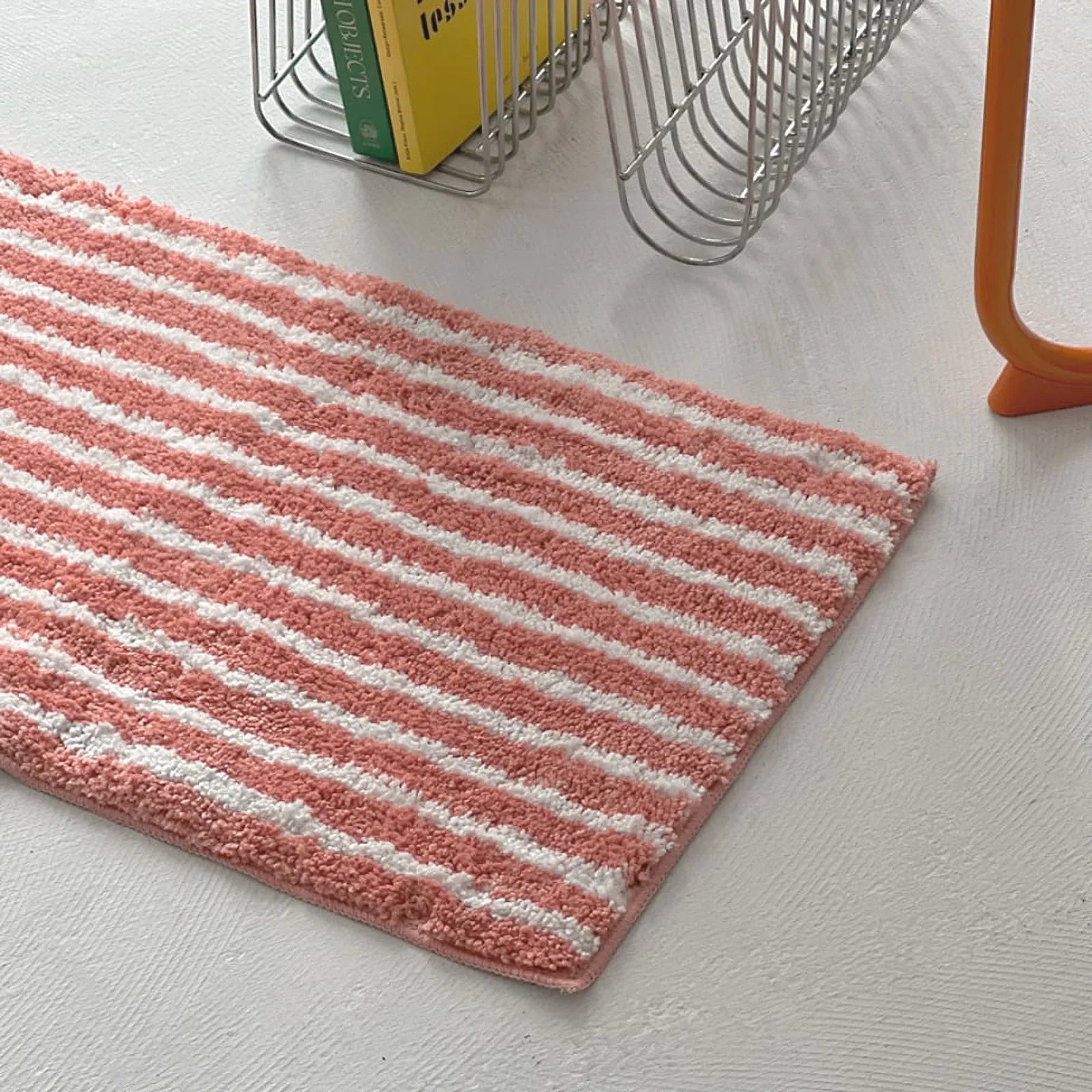 Close up texture of pink tufted rug next to yellow book and orange chair - RoomDen