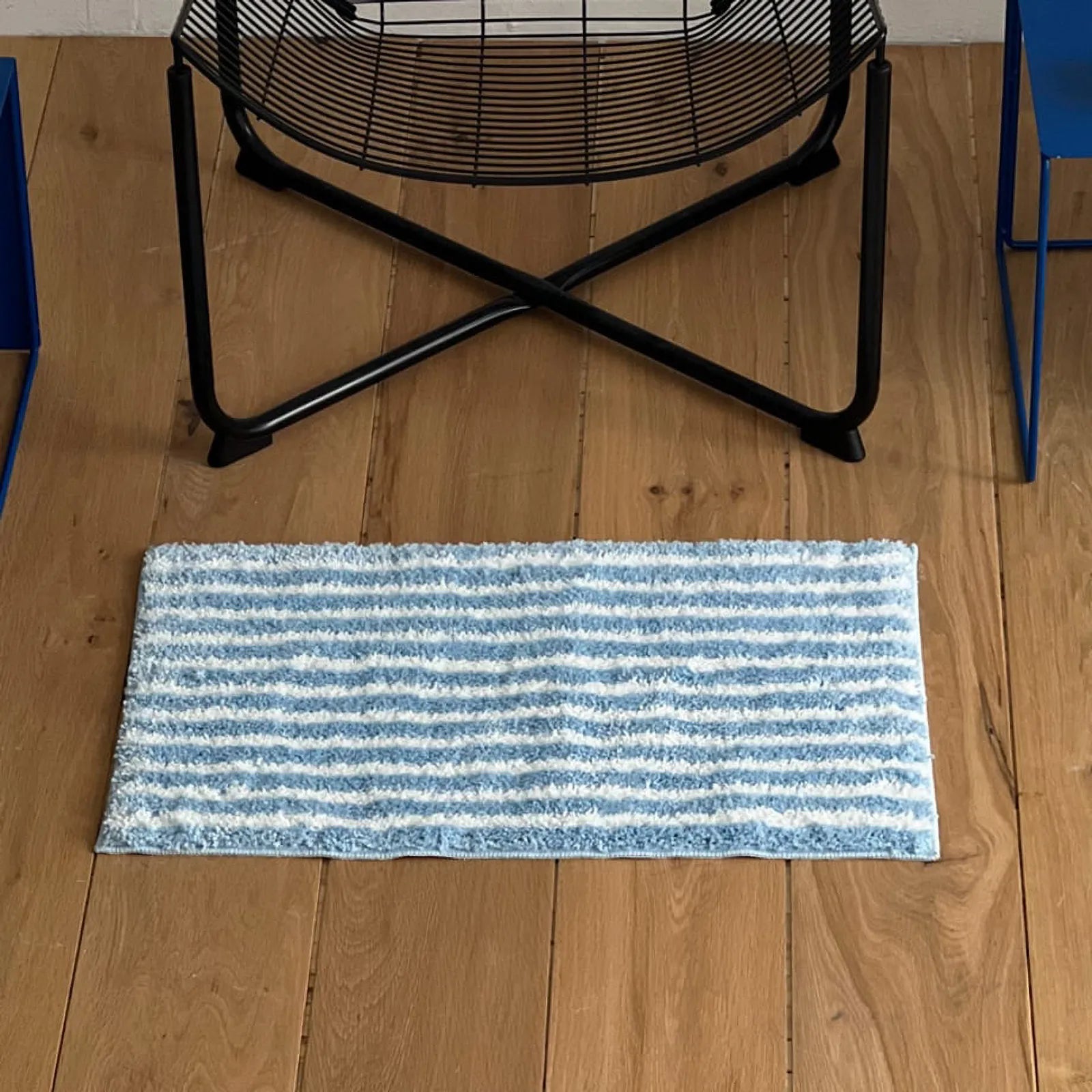 Blue irregular stripe shaggy rug placed under a black wire chair - RoomDen