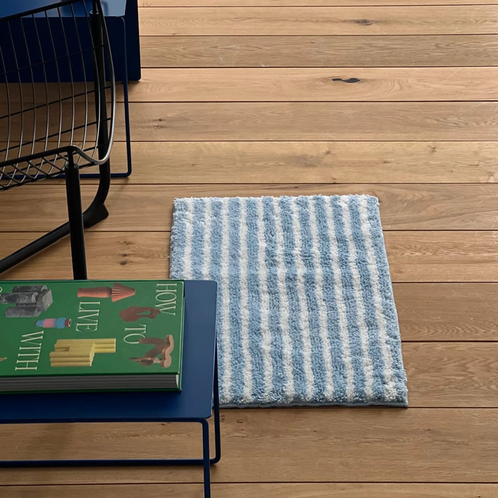 Top view of blue and white striped rug on oak flooring with green book - RoomDen