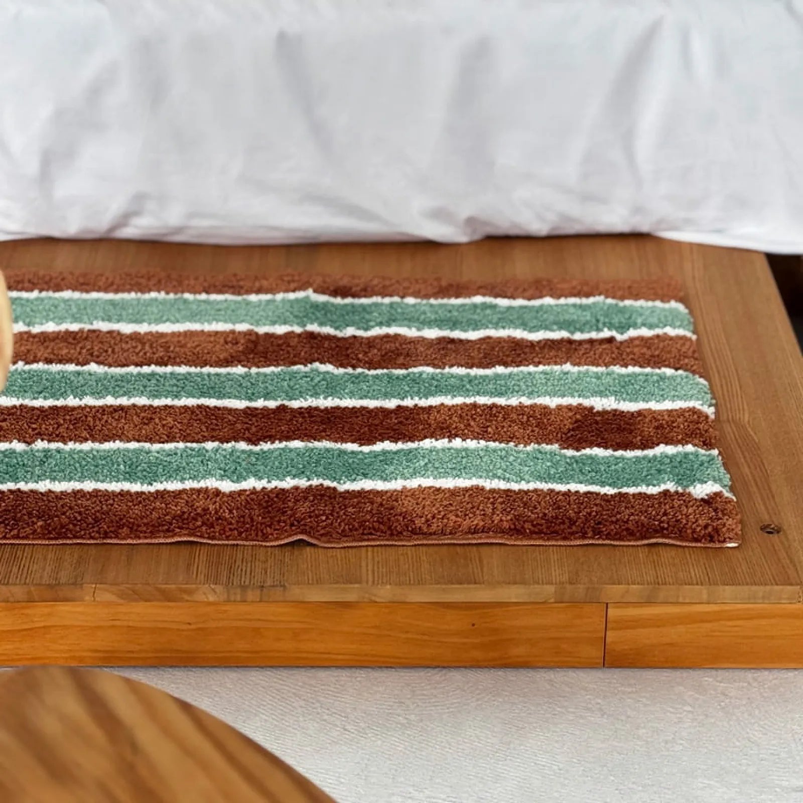 Close-up of the plush texture of a green and brown striped rug on a wooden surface.