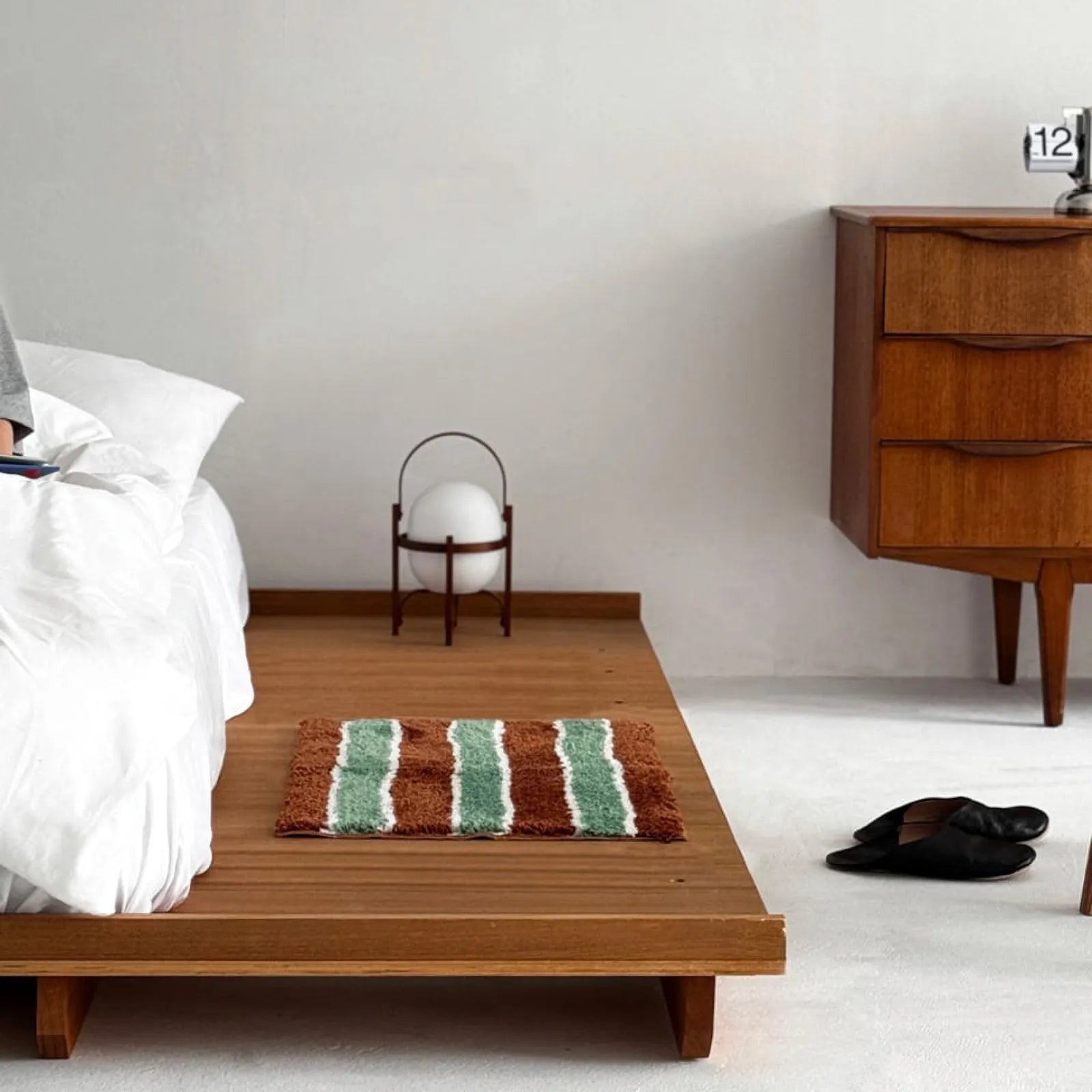 Soft tufted accent rug with green and brown stripes placed beside a bed on a wooden platform.