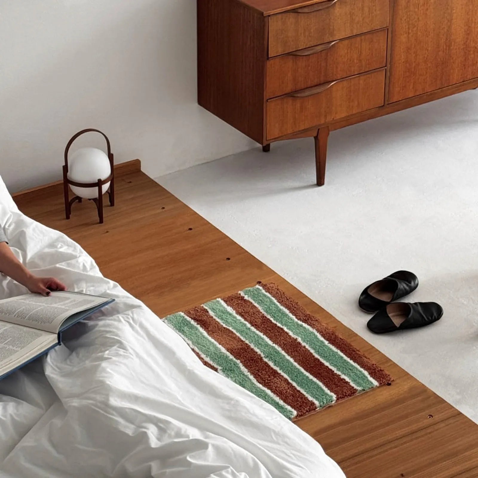 Bedroom scene featuring a striped accent rug near a mid-century modern dresser and low bed.