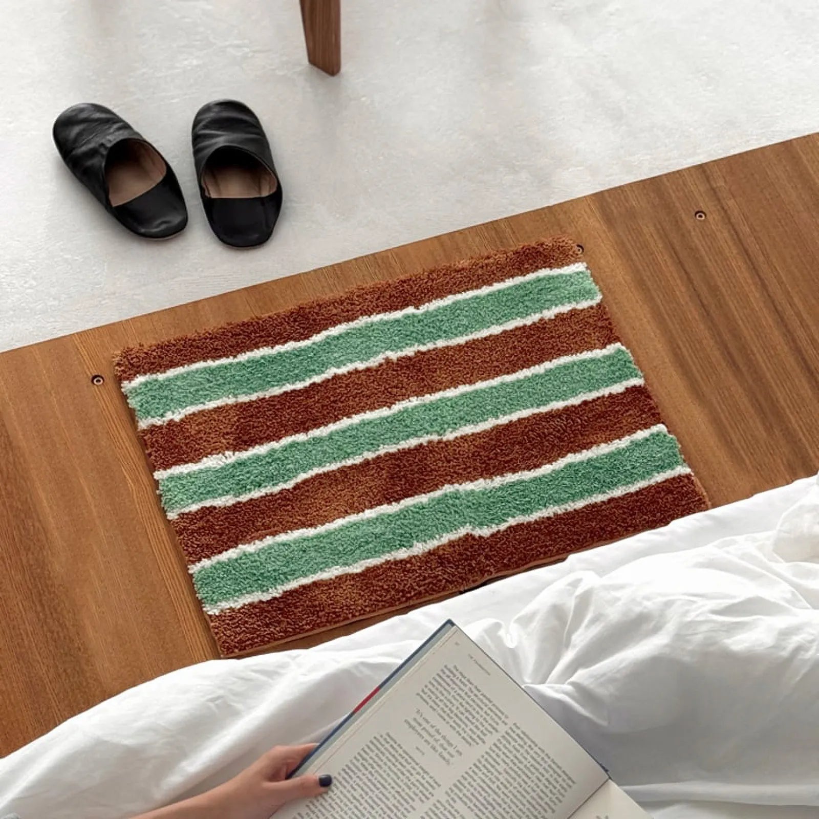 Top-down view of a retro striped rug in sage green and rust brown on a wood floor near slippers.