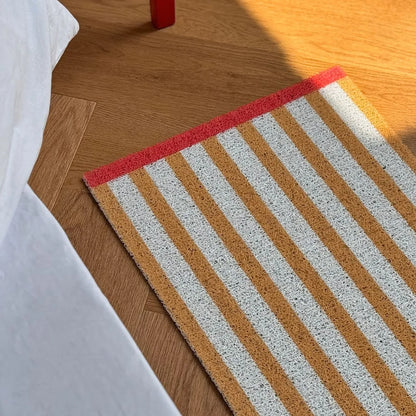 RoomDen Sunshine Yellow striped coil mat placed on a wooden floor in sunlight.