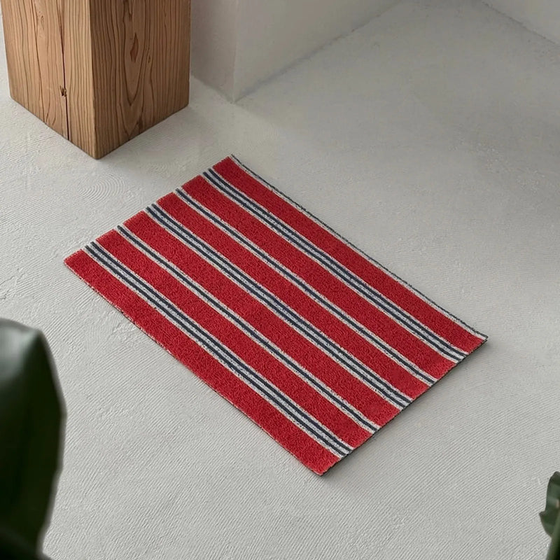 Angled view of a red, blue and white striped PVC coil rug showing its flat profile - RoomDen