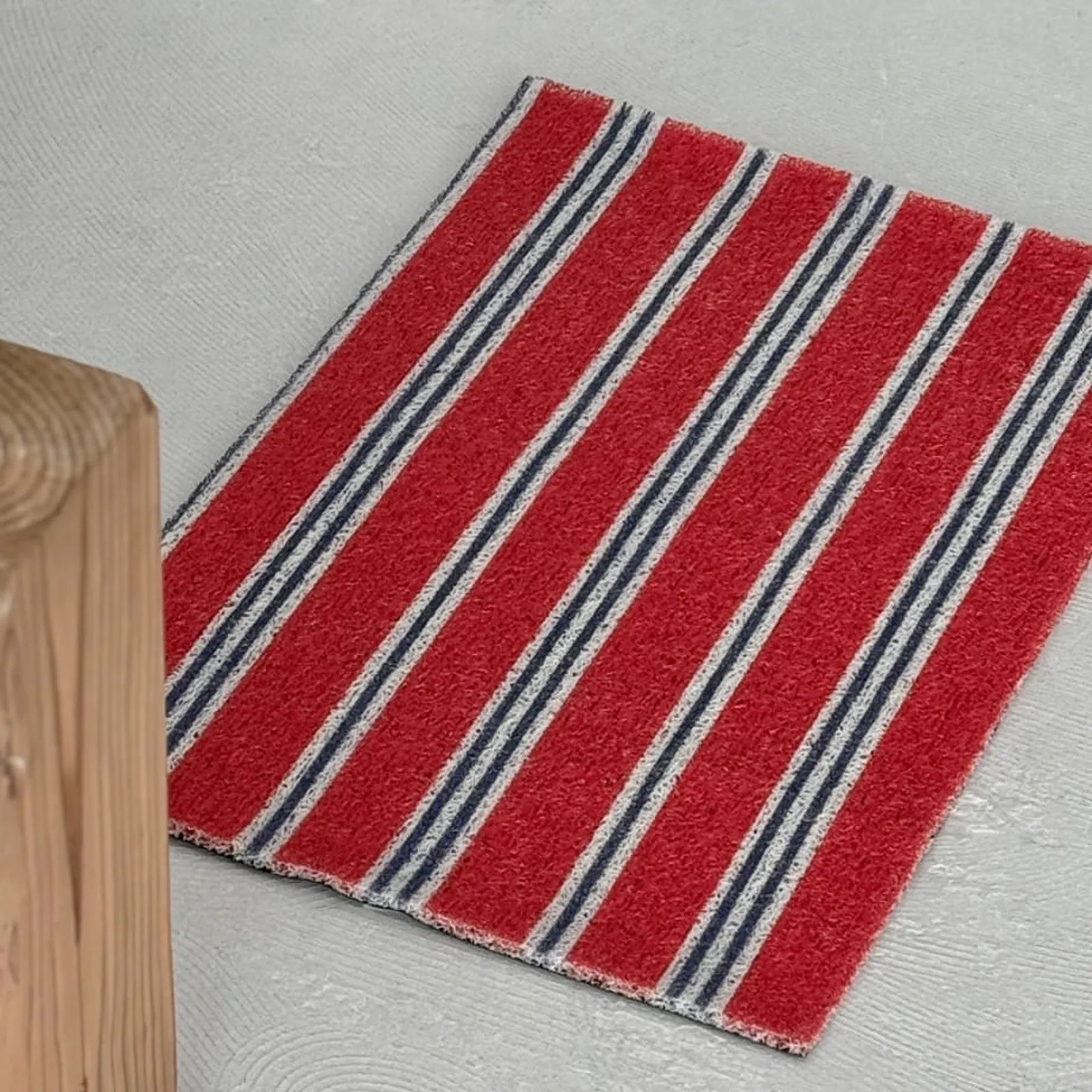 High-angle shot of a retro Americana red coil rug placed near a raw wooden block - RoomDen