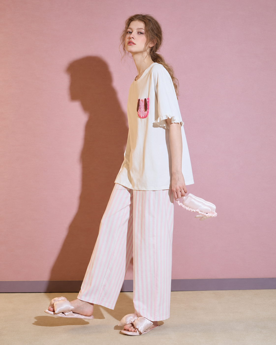 Side standing view of the loose white top and full-length striped pants