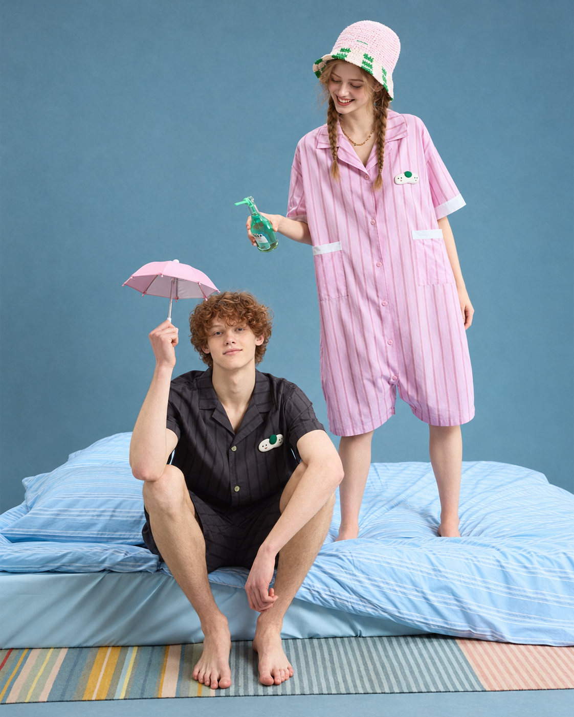 Front view of pink striped cotton one-piece pajamas worn standing on a bed.