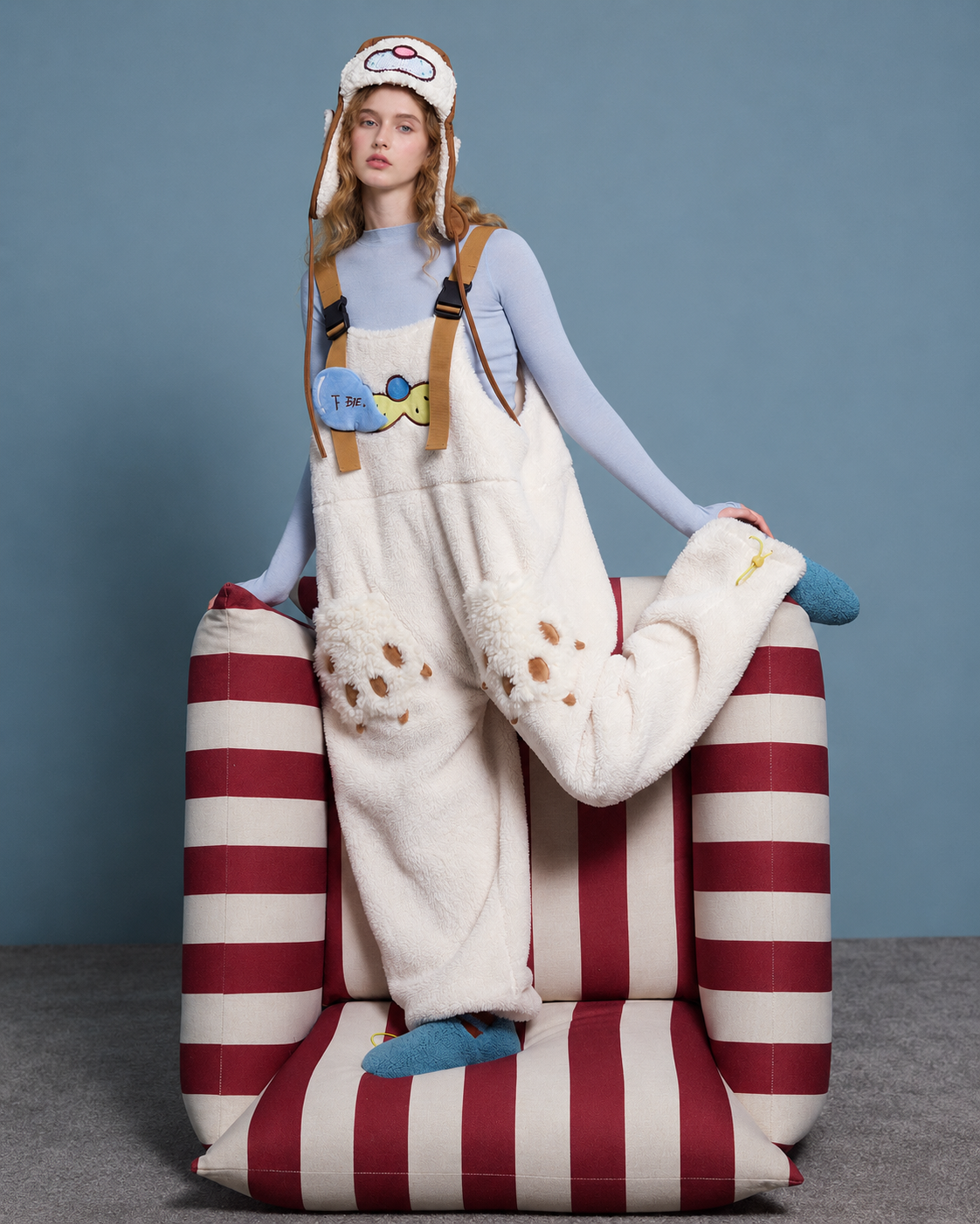 Cat-paw plush one-piece pajamas – cream bent-leg pose on striped armchair - Roomden