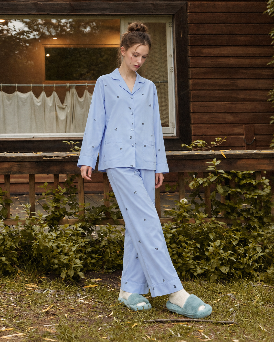 Animal-embroidered cotton pajama set in Sky Blue, standing outside a wooden cabin - Roomden