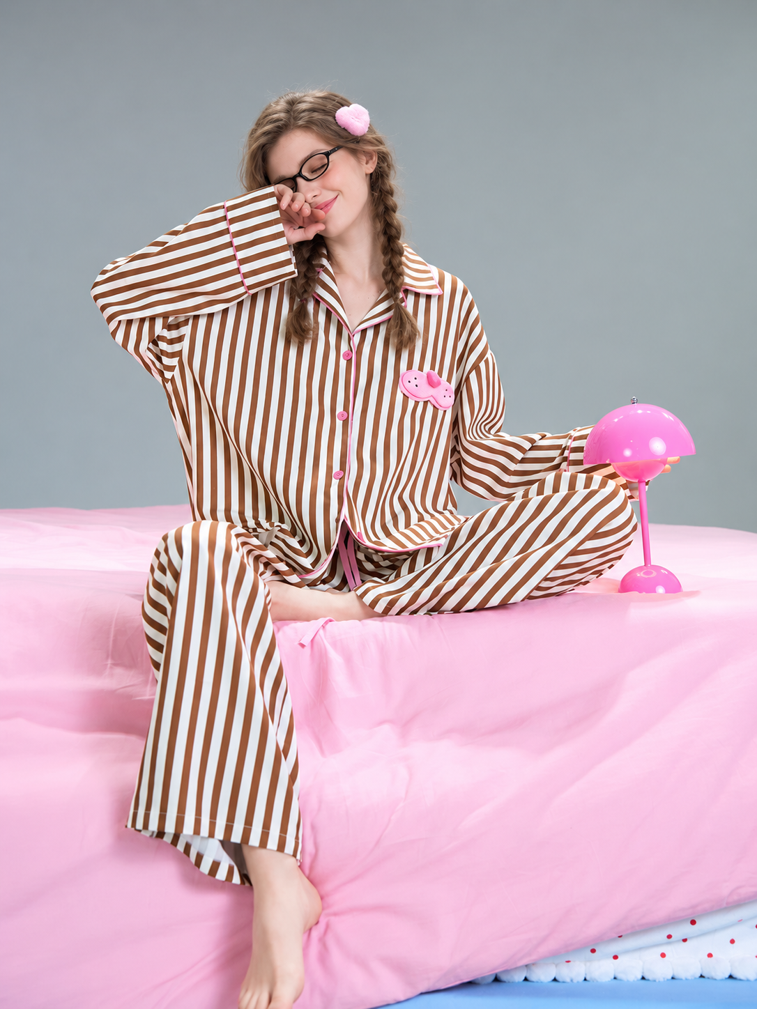 Striped Cat-Patch Pajama Set – Mocha Brown seated on the bed beside a pink lamp - Roomden
