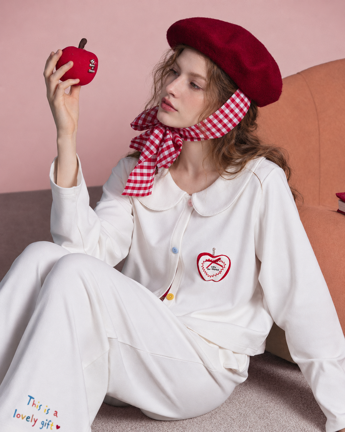 Seated view of the ivory apple-detail pajama set.