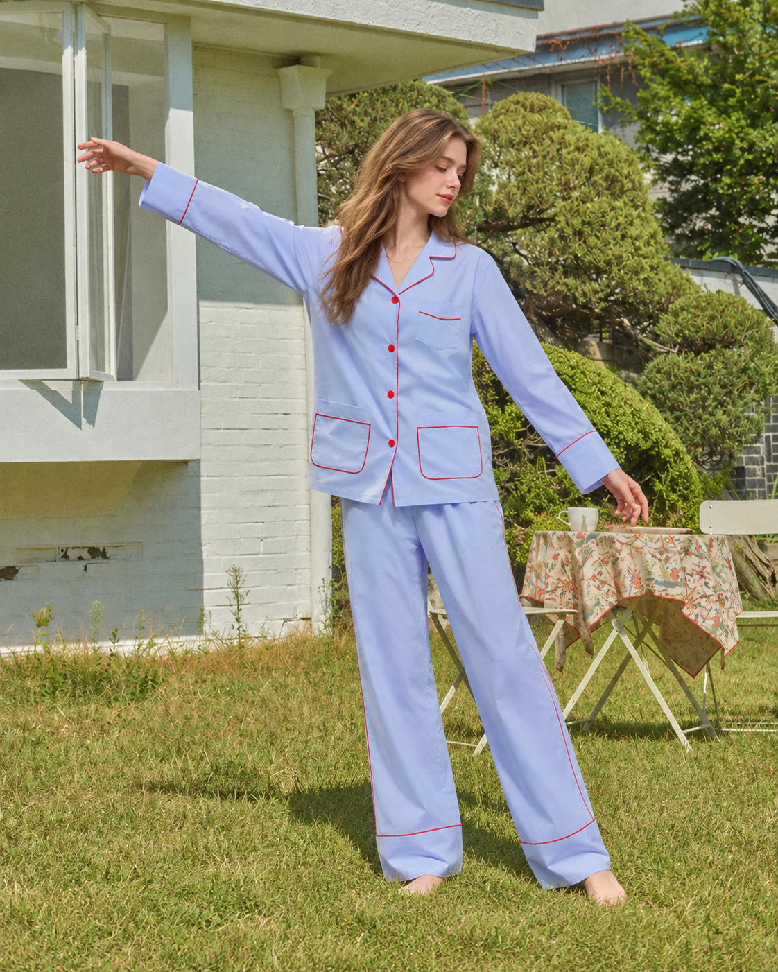 Linehaven contrast-piped pajama set in blue, standing with arms extended in the garden - Roomden