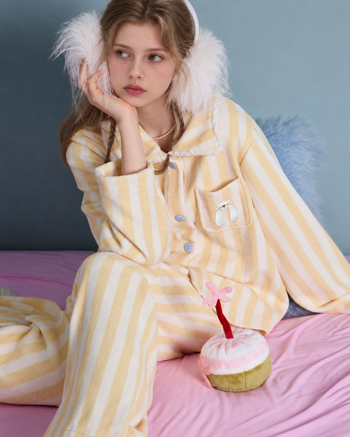 Striped fleece pajama set – seated on a pink bed with hand resting under chin - Roomden