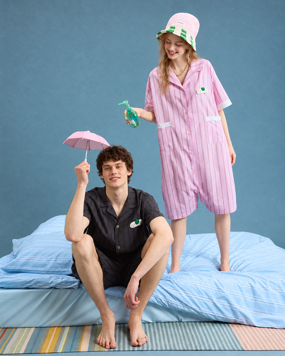 Men's Pinstripe Cotton Pajama Set – charcoal short set, seated at the edge of a blue bed - Roomden