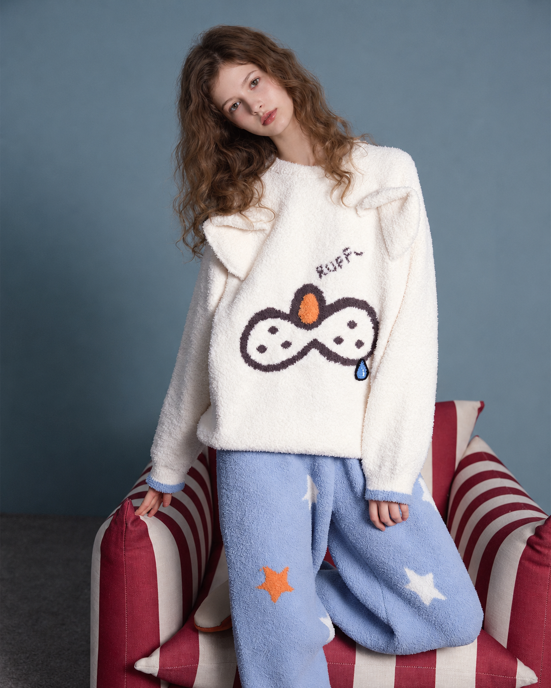 Cat & Star Plush Pajama Set – ivory cat-face top and blue star trousers, leaning beside a striped chair - Roomden