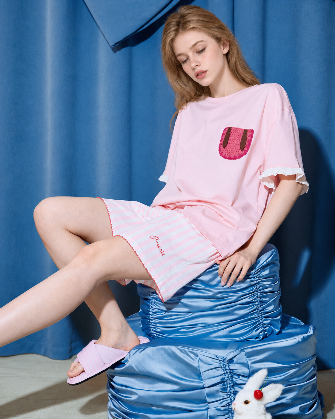 Flopnote Pink Rabbit-Pocket Cotton Pajama Set – crossed-leg seated view on a blue cushioned stool - Roomden