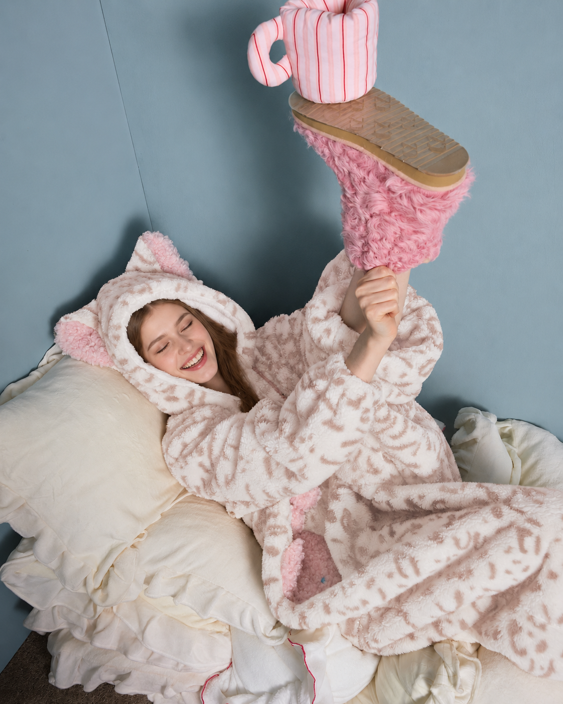 Cat-Ear Leopard Fleece One-Piece Pajamas – cream and pink reclining pose beside pillows - Roomden