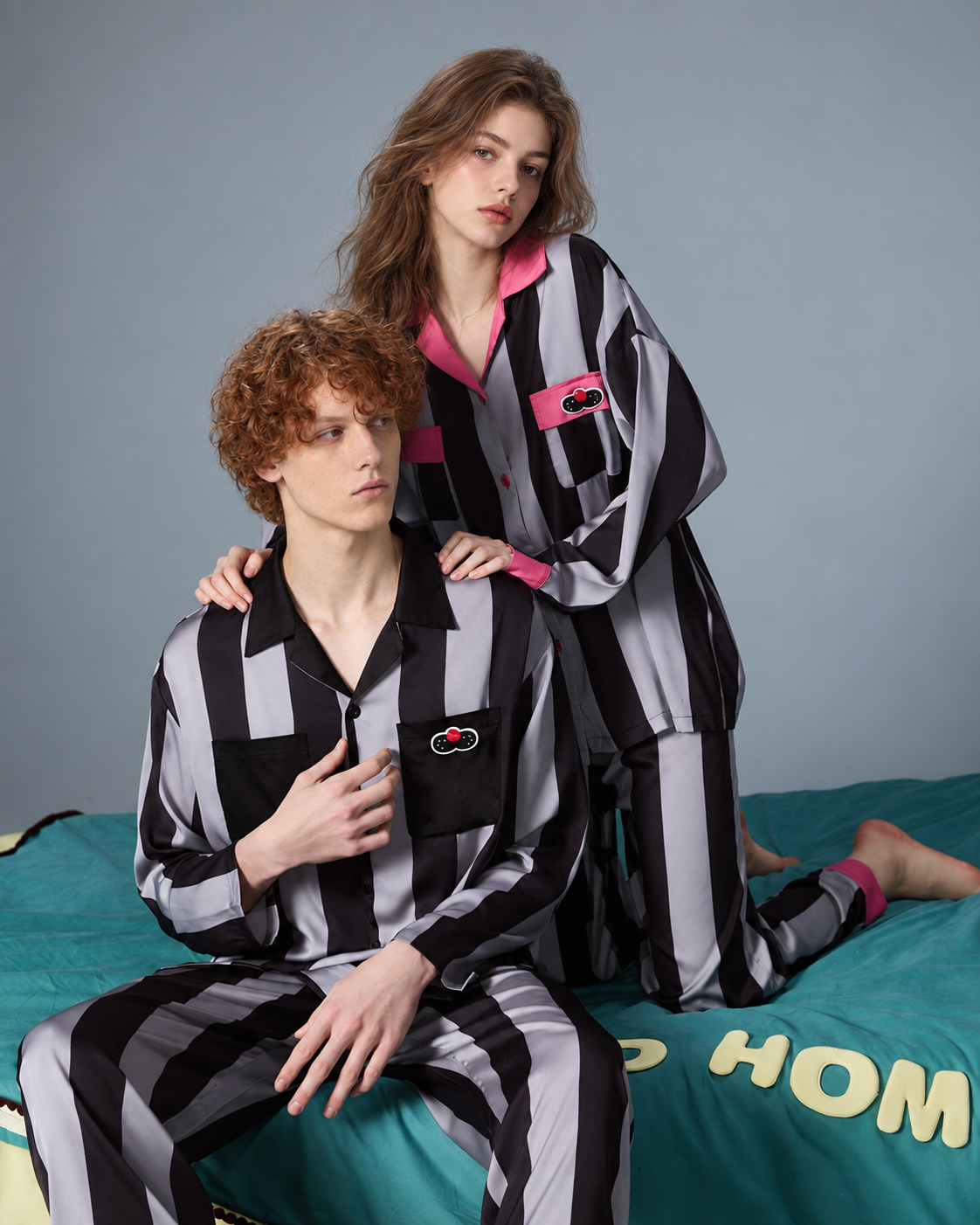 Women's striped pajama set – pink-trim sleeves and trousers shown kneeling on a teal bed - Roomden