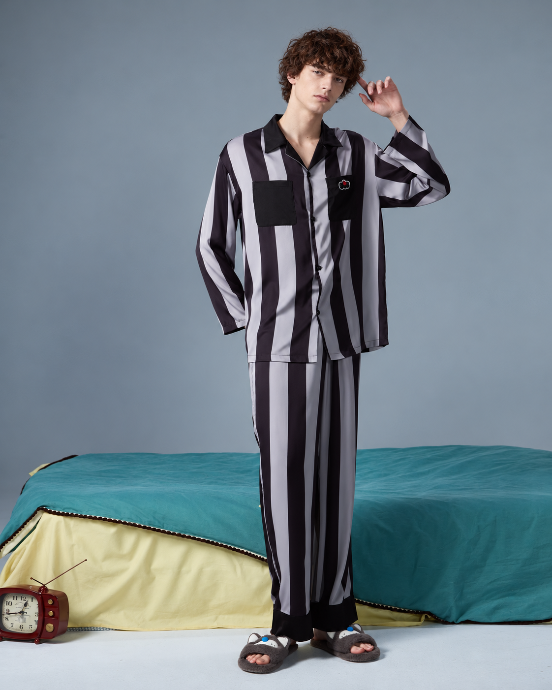 Men's striped pajama set – full shirt and trousers shown standing beside a teal bed - Roomden