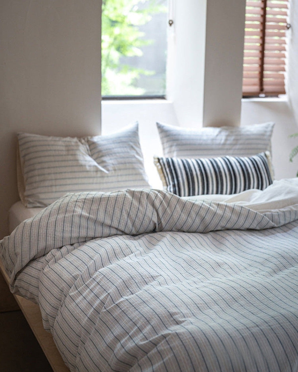 Winslet Pinstripe Cotton Bedding Set – matching striped pillows and folded duvet beside a window - Roomden