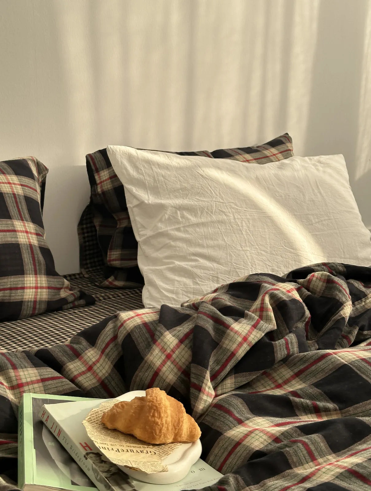 Close up detail of vintage plaid duvet cover texture with croissant on bed | RoomDen