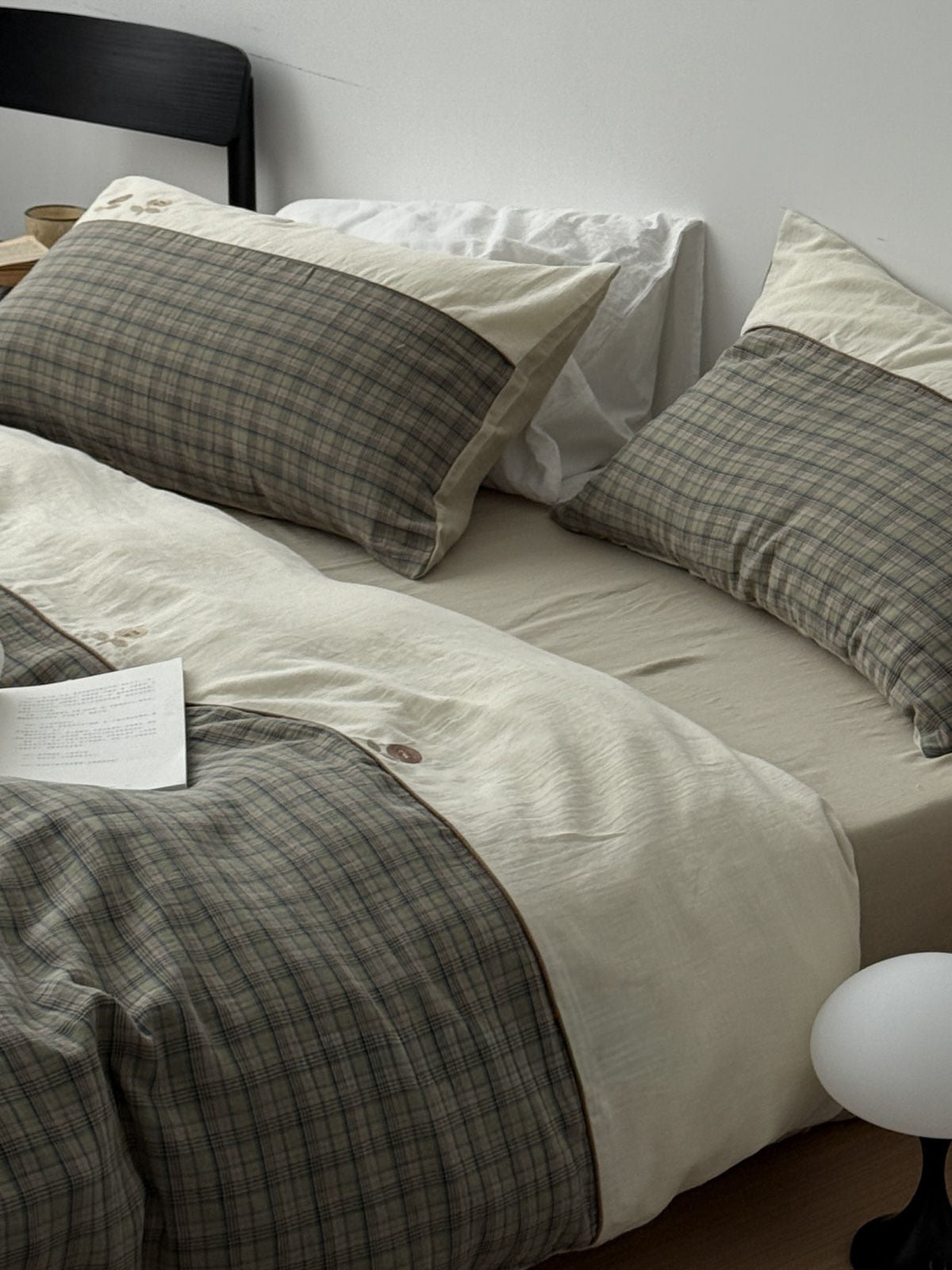 Close up of sage green plaid duvet cover paired with cream floral embroidered pillows in a cozy bedroom. | RoomDen