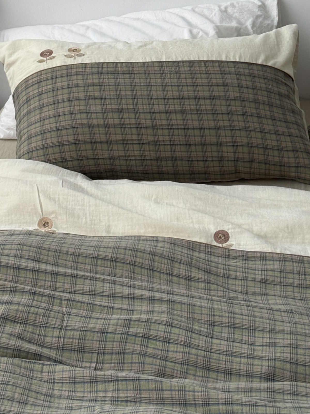 Top view of patchwork bedding design featuring cream top with embroidery and green plaid bottom. | RoomDen