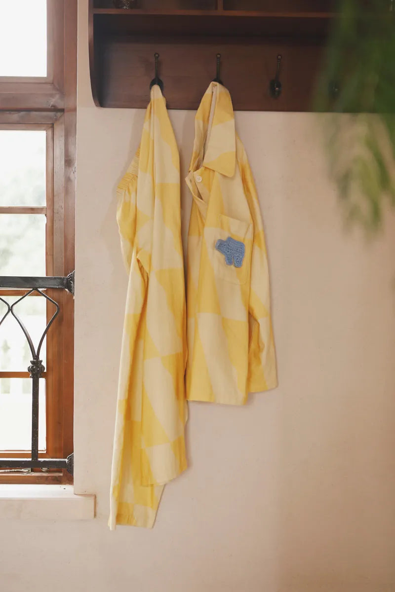Yellow checkered cotton pajama top and pants hanging on wall hooks in a warm cozy room – RoomDen