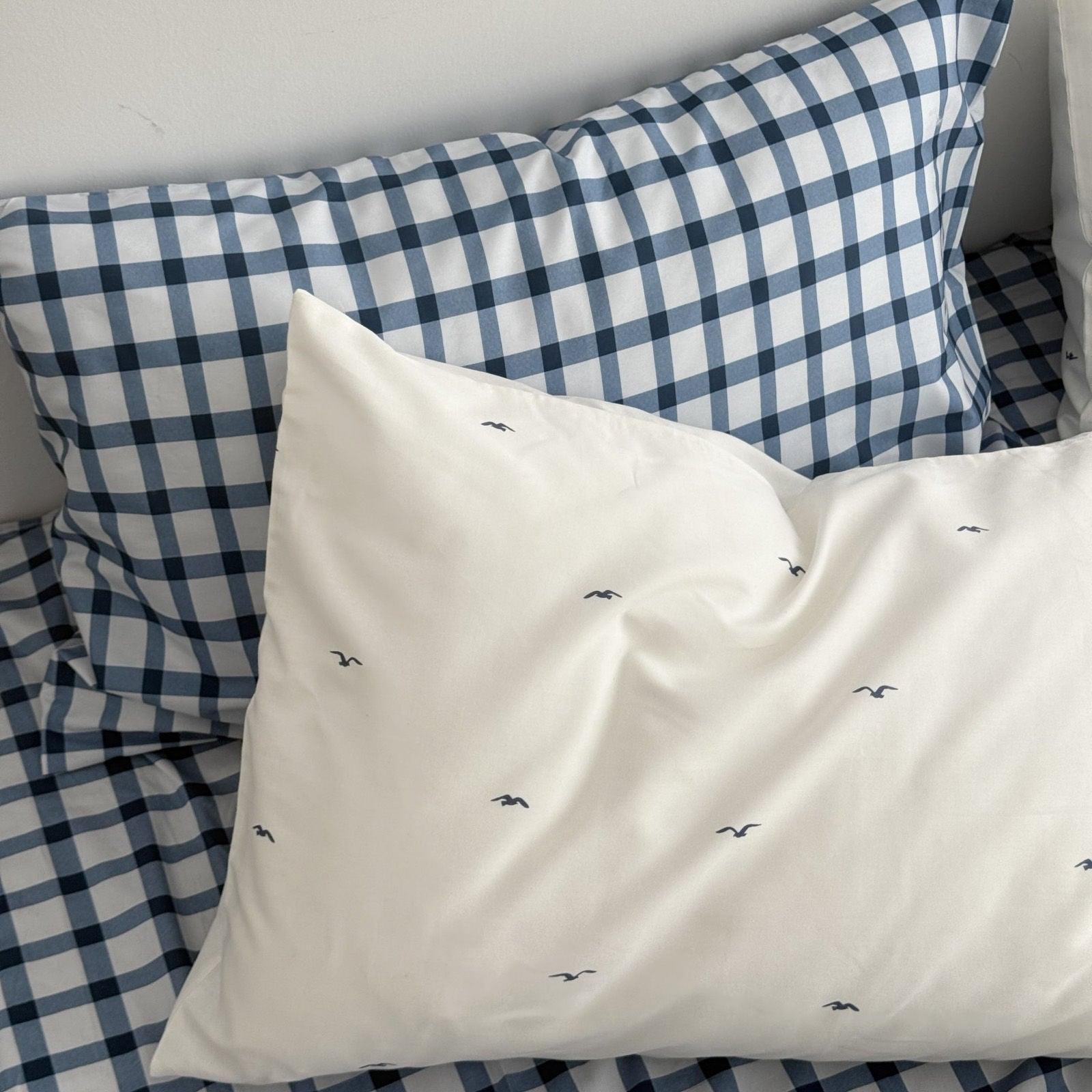 Close up of white pillowcase with flying bird pattern against blue checkered sheet background