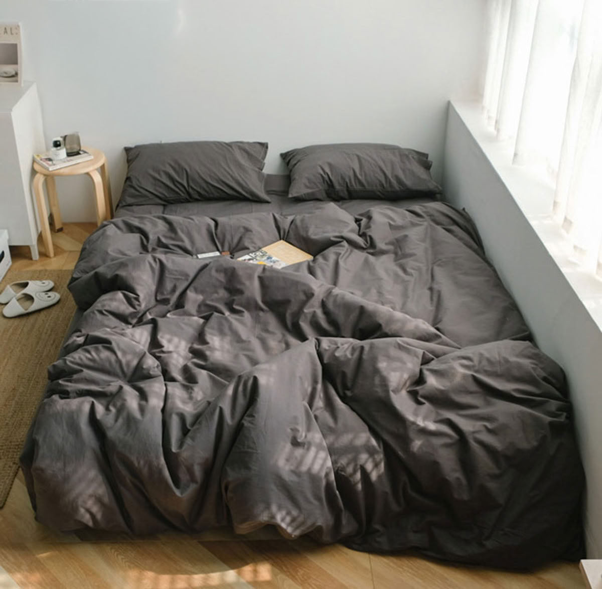 Minimalist brown grey washed cotton bedding set in a bright bedroom with sunlight filtering through curtains - RoomDen