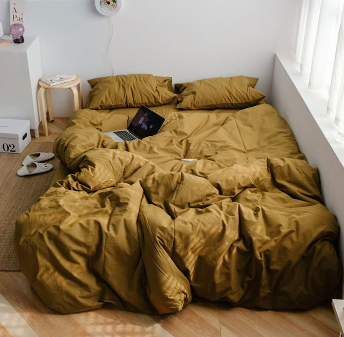 Warm mustard yellow washed cotton bedding set in a minimalist bedroom with wooden floor and sunlight - RoomDen
