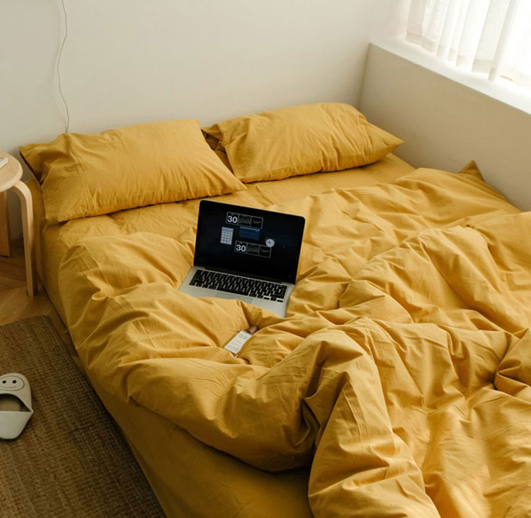 Sunny yellow washed cotton bedding set with matching pillows and laptop on the bed - RoomDen 