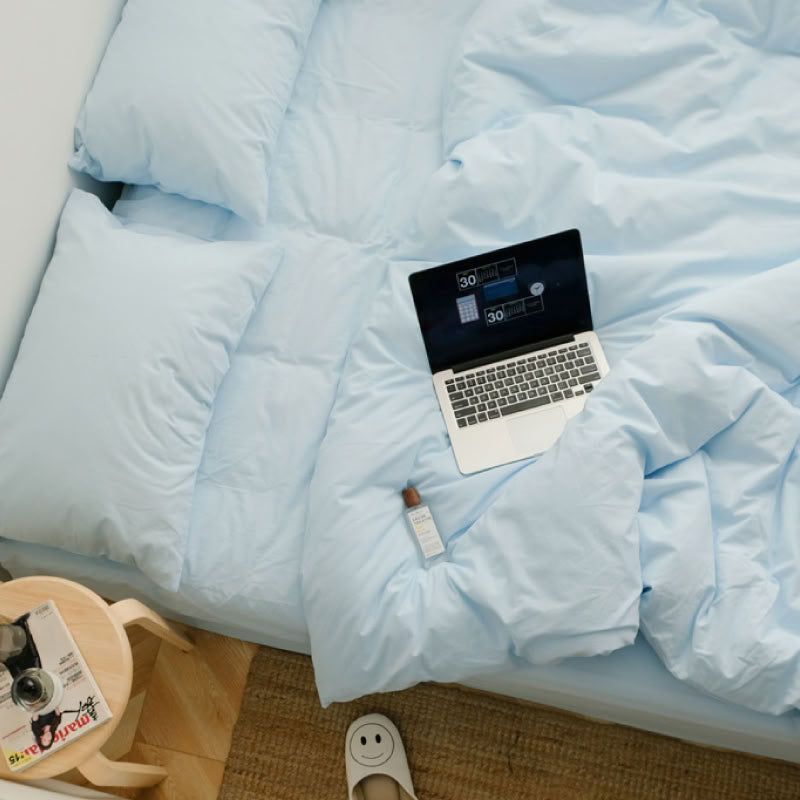 Sky blue washed cotton bedding set with matching pillows and a laptop on the bed - RoomDen