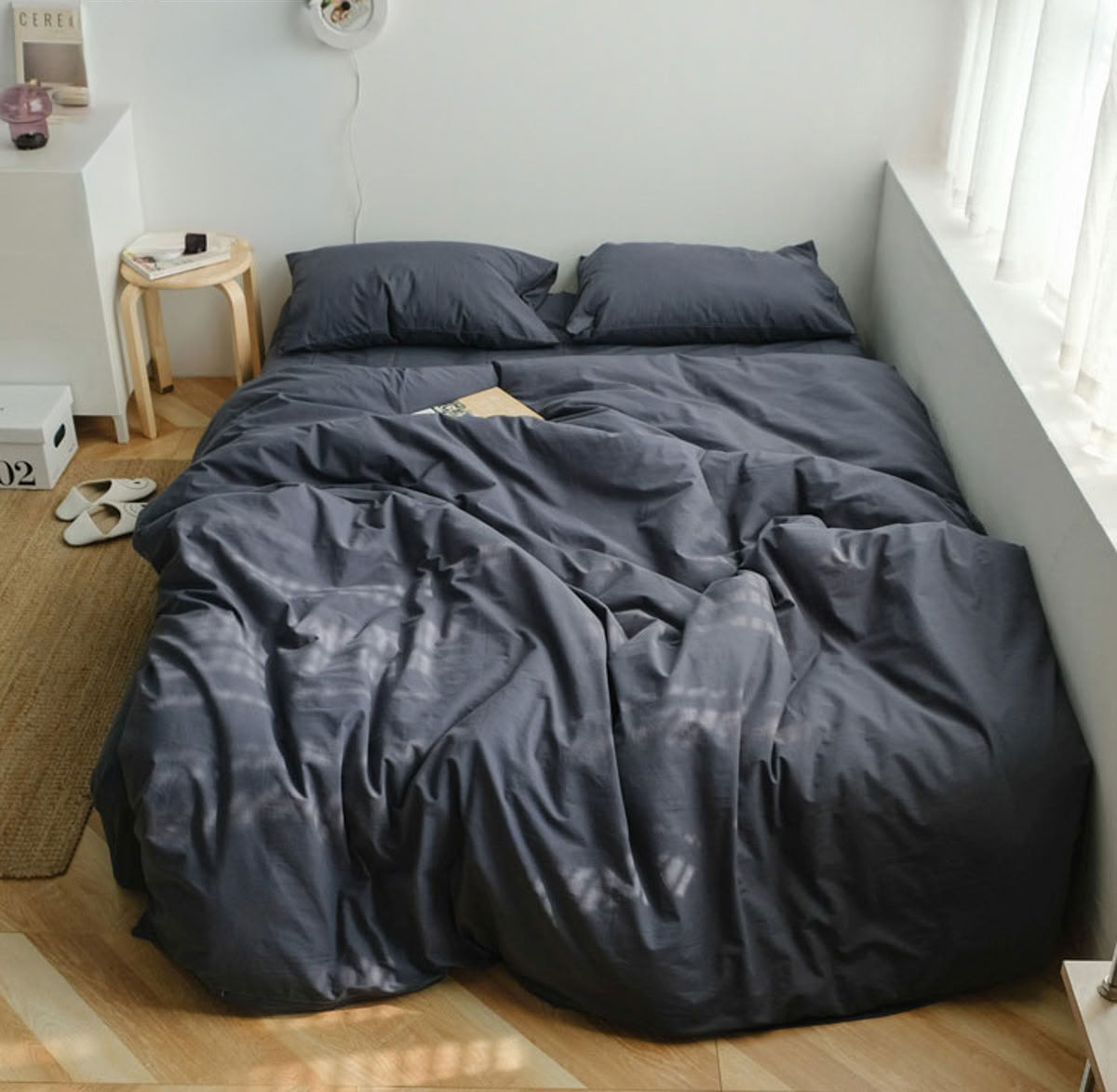 Minimalist blue grey washed cotton bedding set in a bright bedroom with natural sunlight and wooden floor- RoomDen