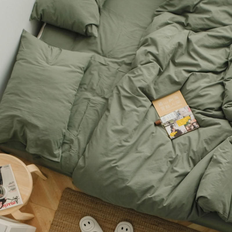 Soft sage green washed cotton bedding set with a book and warm natural light - RoomDen