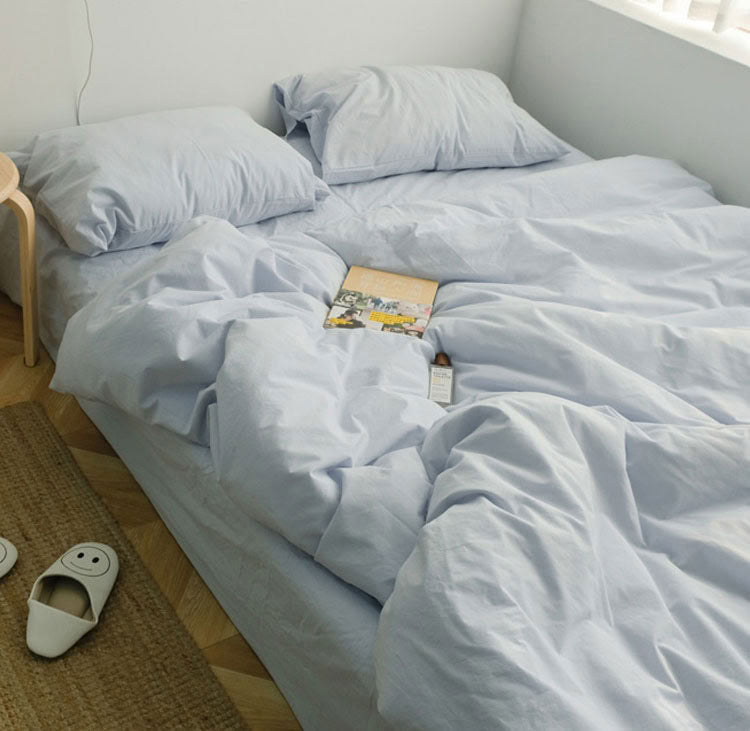 Light blue washed cotton bedding set with soft pillows on a low bed near the window - RoomDen