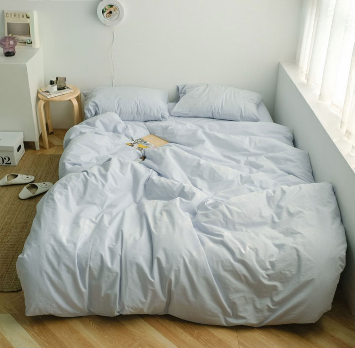 Minimalist light blue washed cotton bedding set in a bright bedroom with white curtains and wooden floor - RoomDen