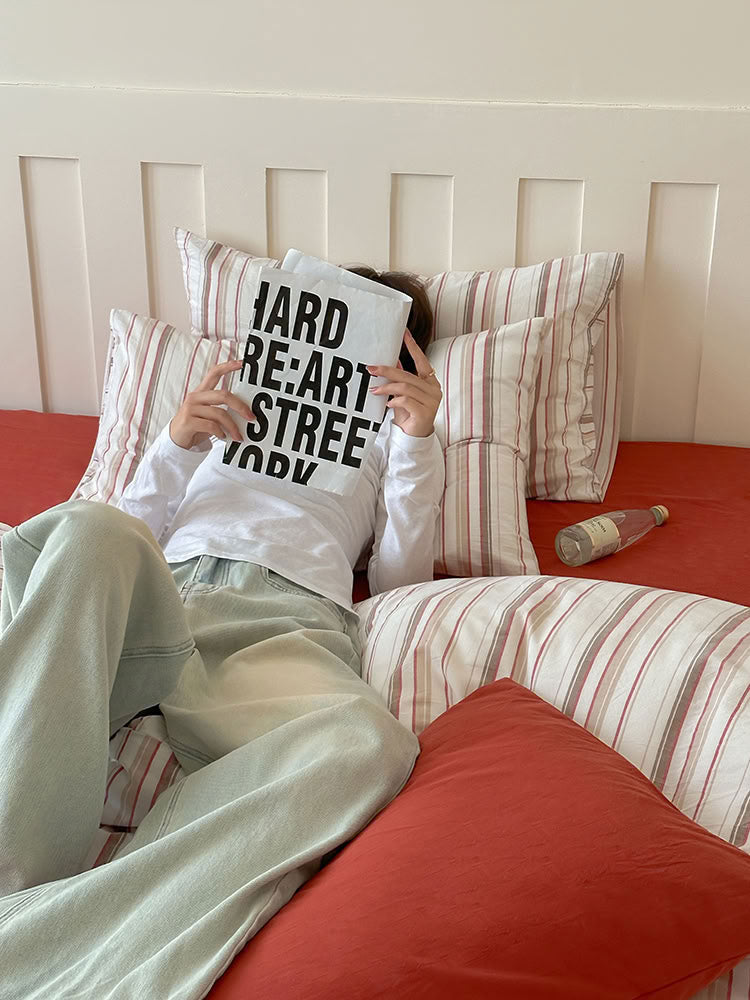 Lifestyle scene with person relaxing on red striped cotton bedding and solid pillowcases – RoomDen
