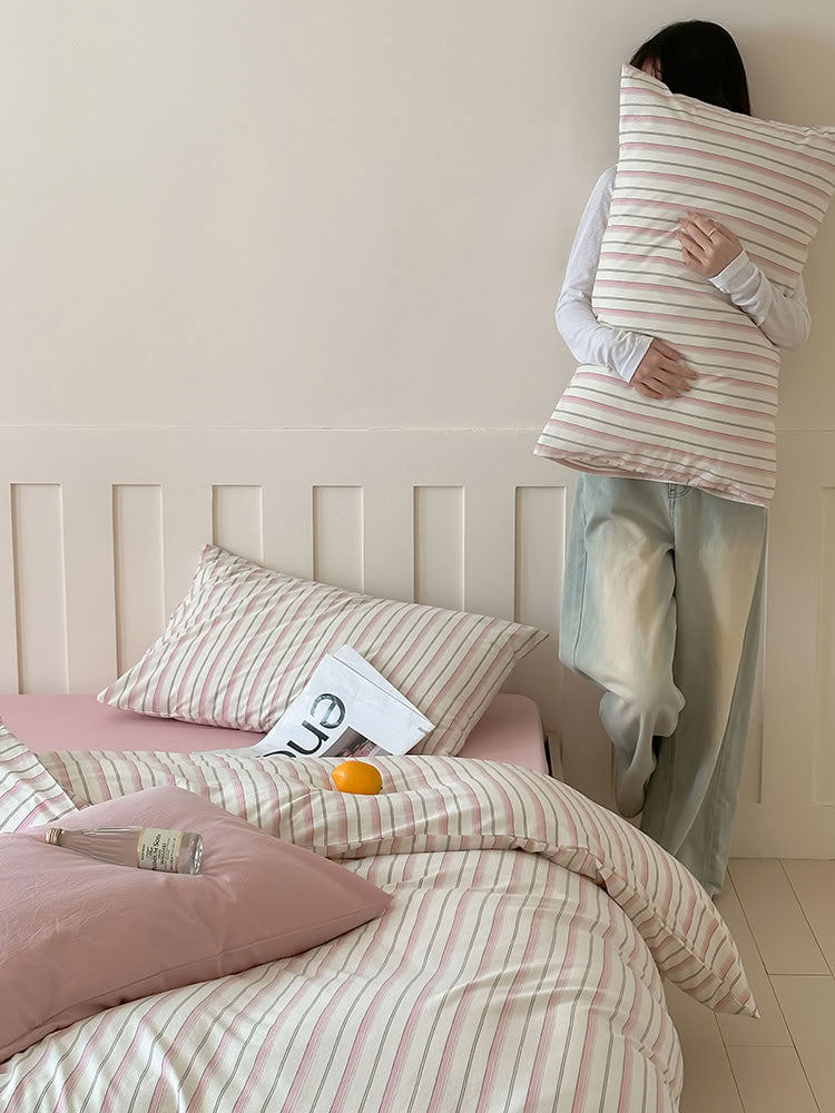 Lifestyle photo with person lounging on pink striped bedding and solid pillow – RoomDen