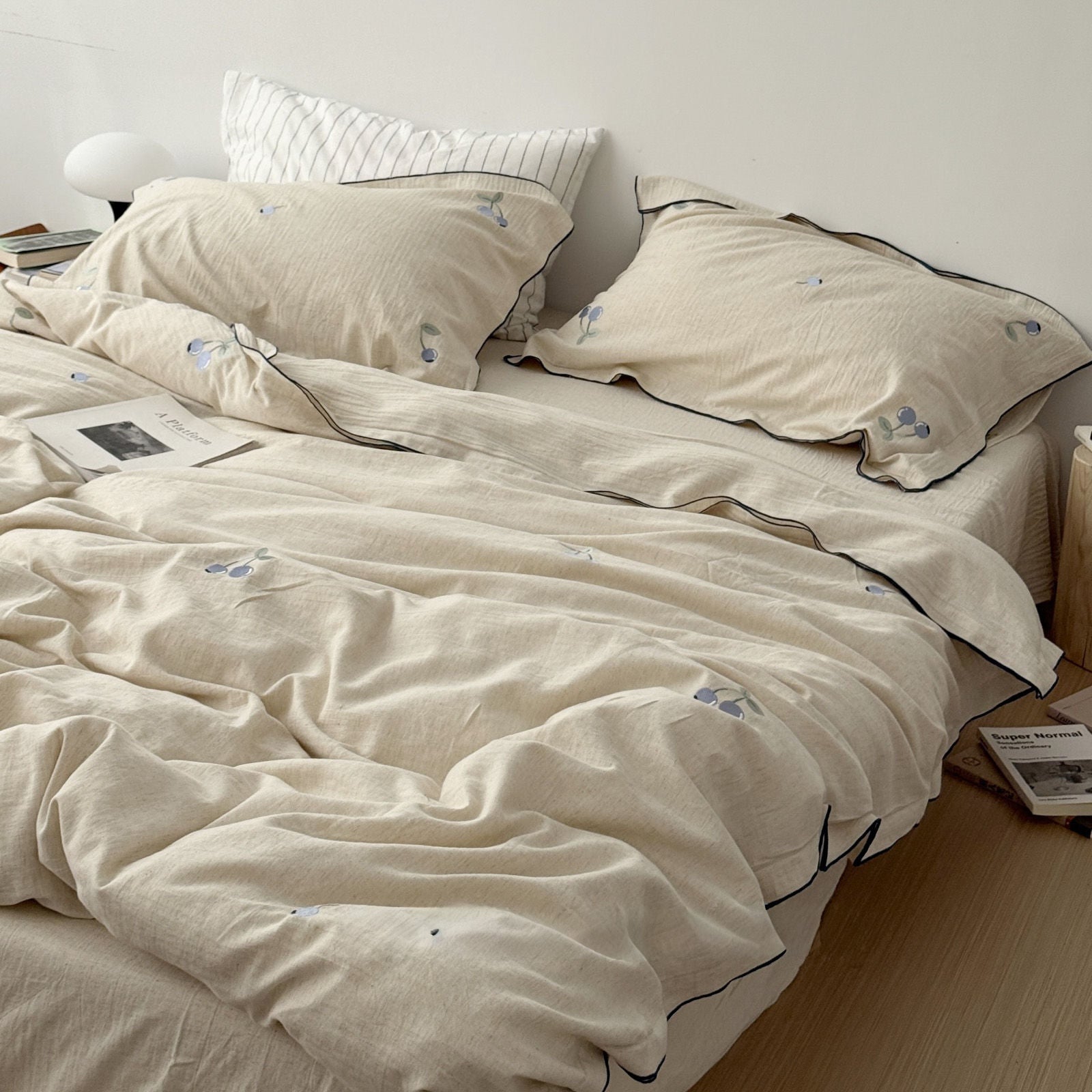 Full view of beige linen bedding set with embroidered blue cherries on a bed, RoomDen cottagecore style.