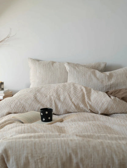 Front view of beige striped bedding set with book and coffee cup styling RoomDen.