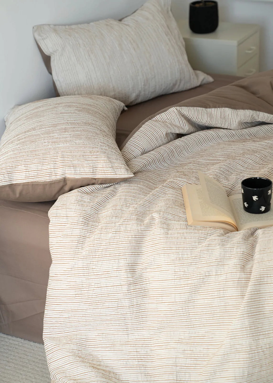 Lifestyle shot of beige striped bedding with open book and candle RoomDen.