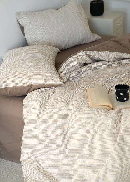 Lifestyle shot of beige striped bedding with open book and candle RoomDen.